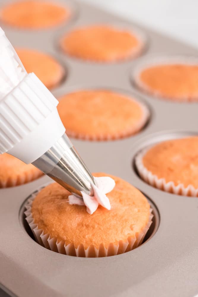 piping frosting onto the pink champagne cupcakes