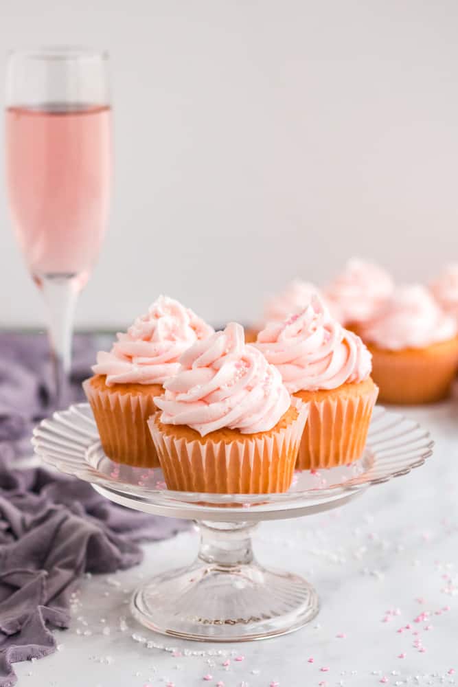 white cake stand with three cupcakes and glass of champagne in background