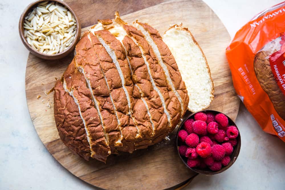 sliced round bread on cutting board with bowl of almonds and raspberries