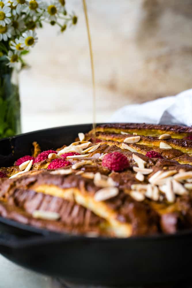 pouring syrup onto raspberry almond baked french toast