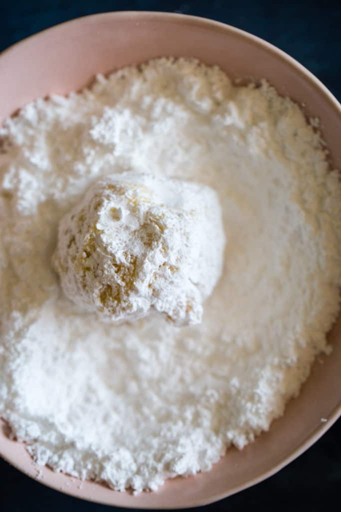 rolling the dough ball in a bowl of powdered sugar