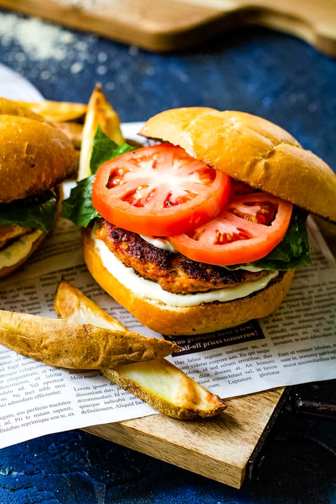 salmon burgers with tomoato slices on board with blue background