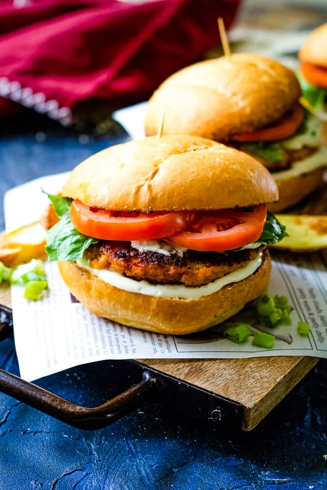 two salmon burgers on wood plank with paper underneath