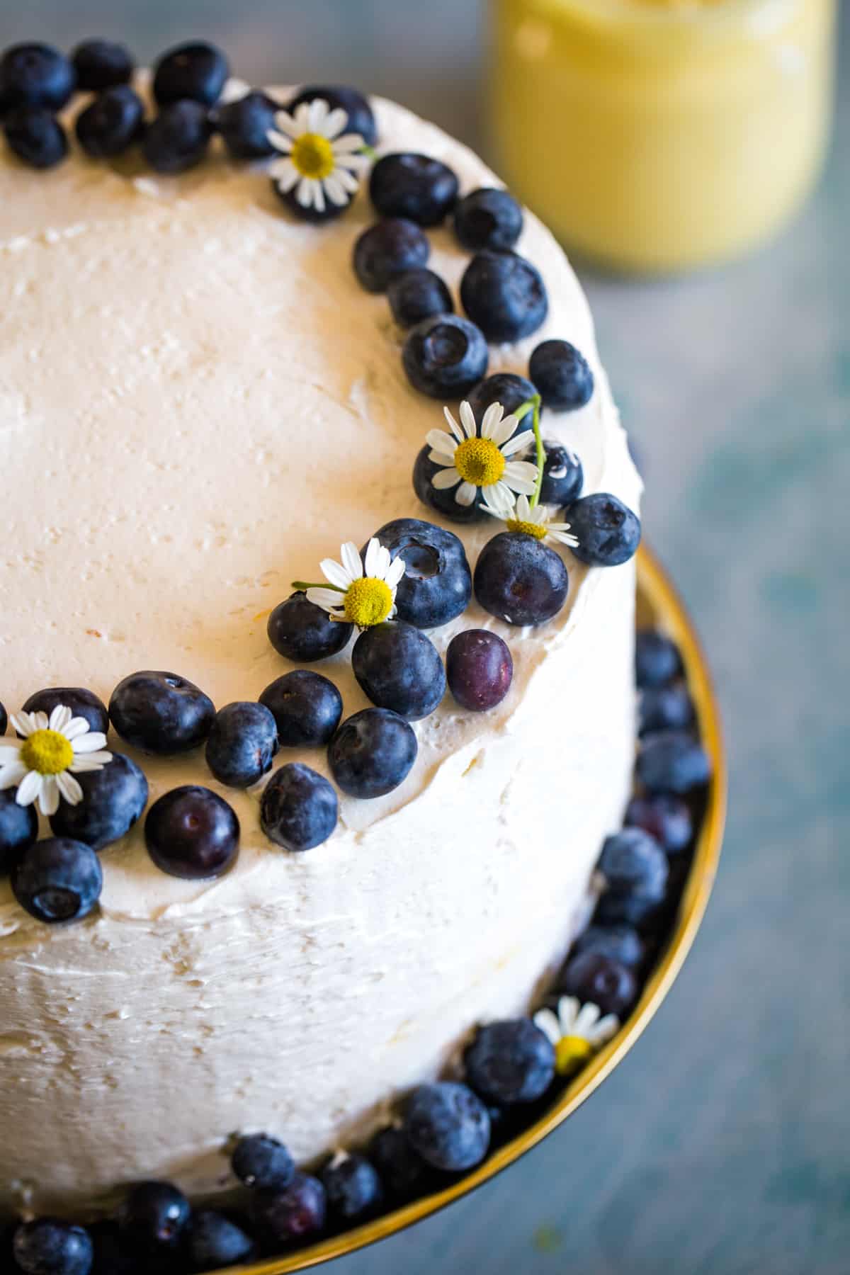 overhead shot of cake with white frosting garnished with fresh blueberries on gold cake platter. 