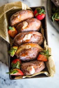 Loaf pan with strawberry custard filled donuts on white marble background