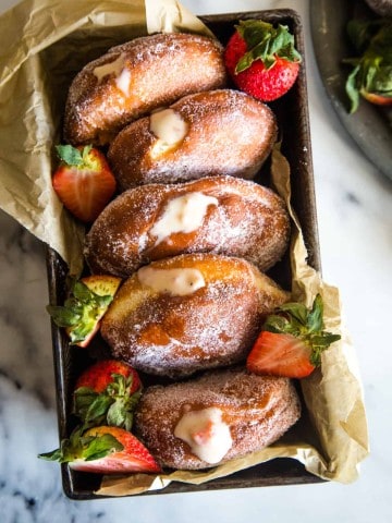 Loaf pan with strawberry custard filled donuts on white marble background