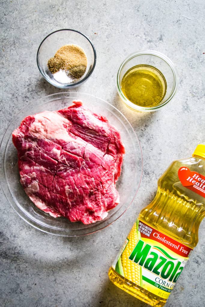 raw flank steak in glass pan with bottle of oil on the side