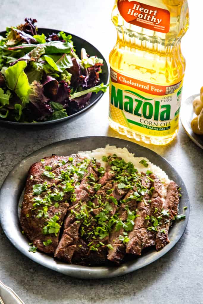 plate with grilled flank steak slices and bottle of oil in background