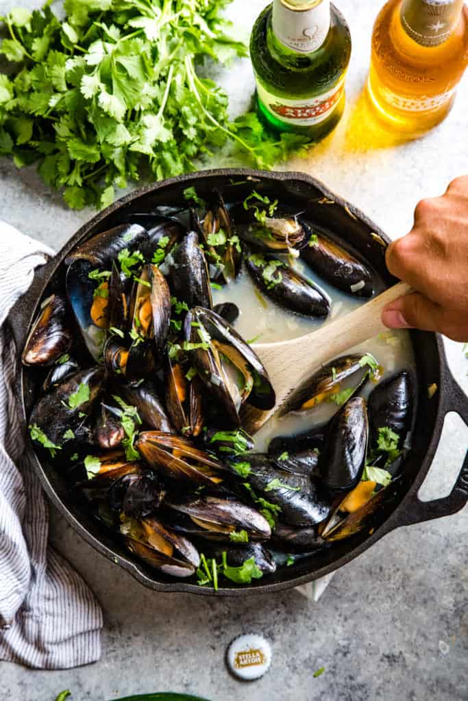 hand scooping out cooked mussels in cast iron skillet