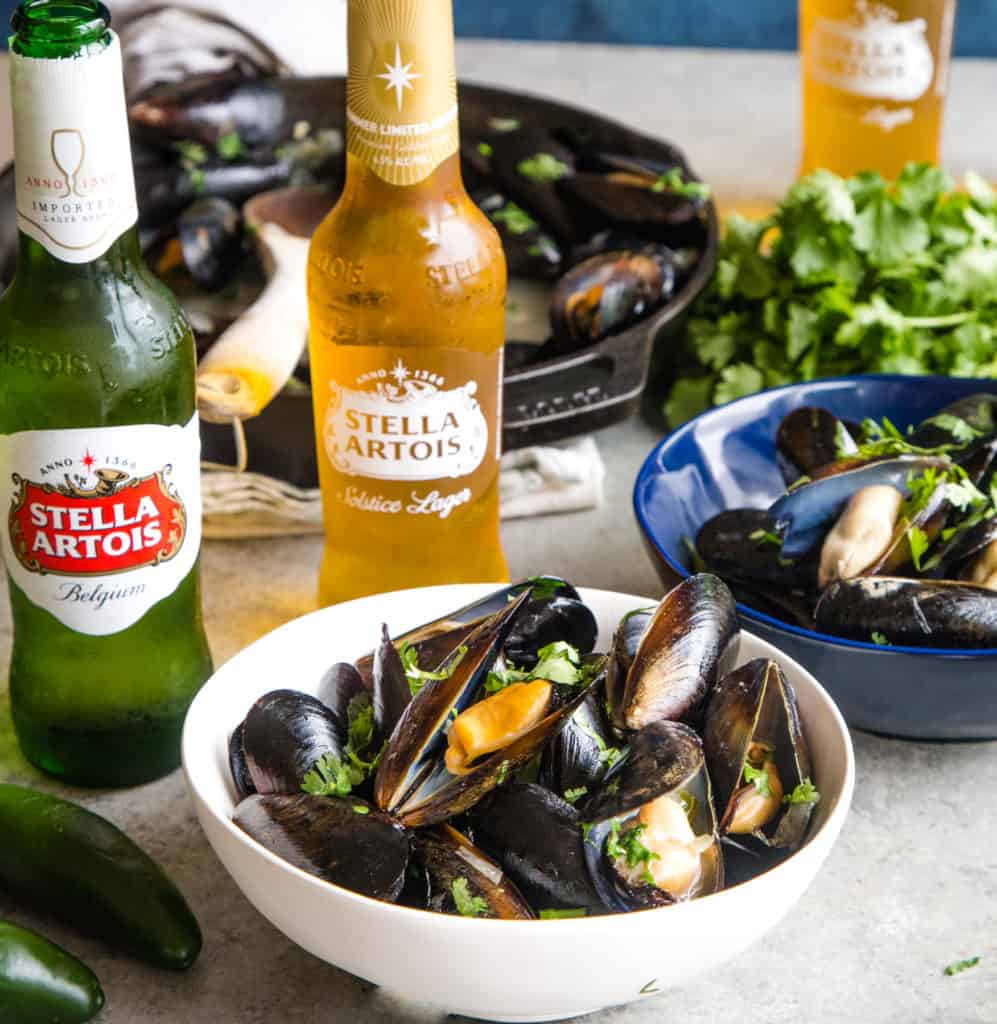 bowls of cooked mussels with bottles of stella artois beer in background