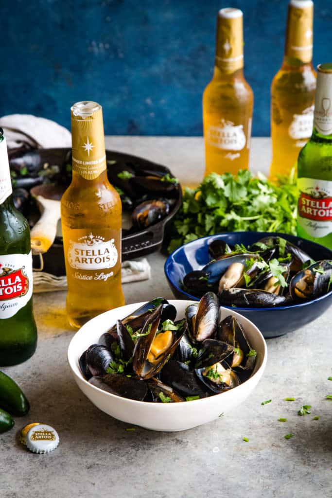 white bowl of cooked mussels with bottles of stella artois in background