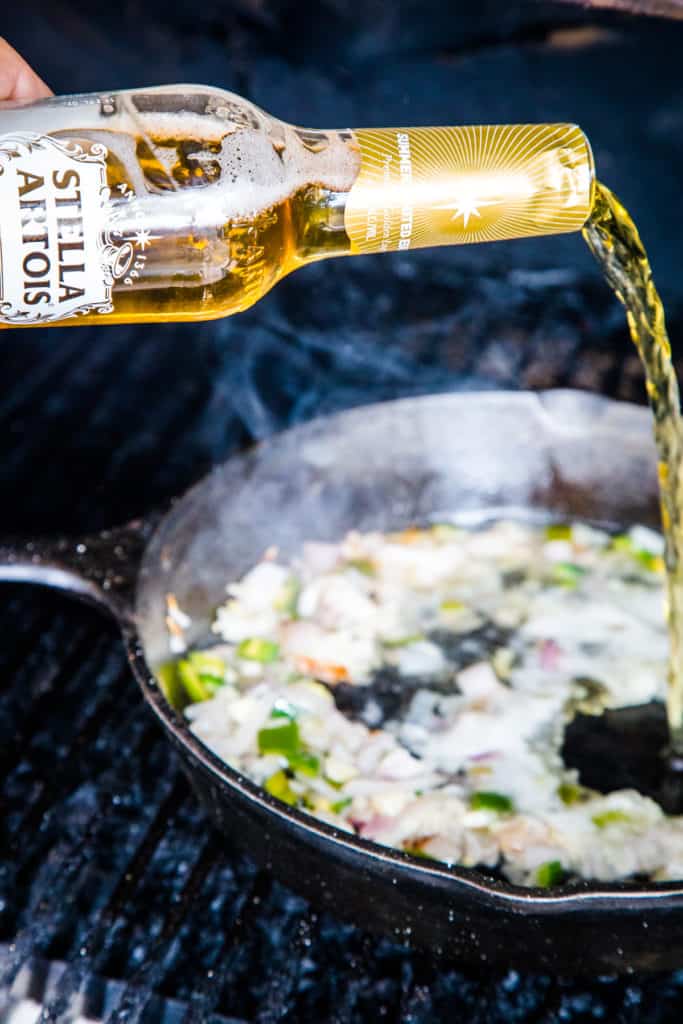 pouring stella artois beer into skillet for broth