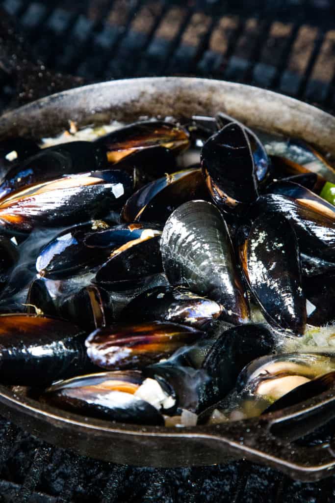 raw mussels cooking in skillet over grill