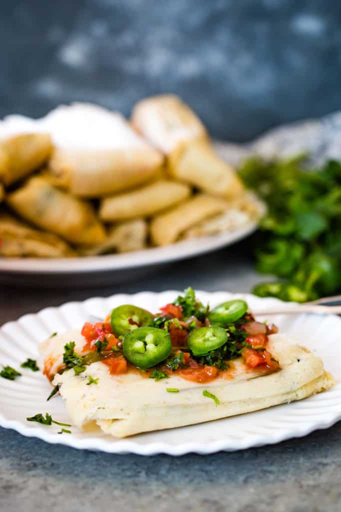 Jalapeño Cheese Tamales on white plate with salsa and jalapeno slices on top as garnish