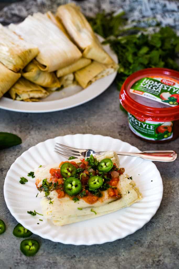 Jalapeño Cheese Tamales on white plate with salsa, jalapeno slices, and cilantro on top as garnish