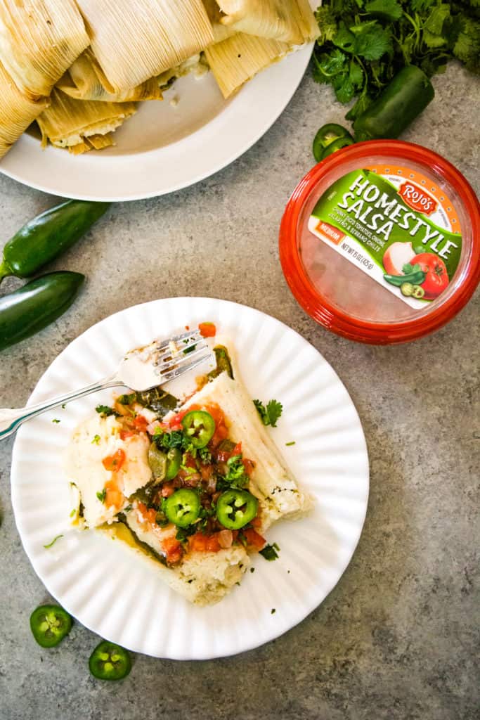 overhead shot of Jalapeño Cheese Tamales on white plate with salsa and jalapeno slices on top as garnish