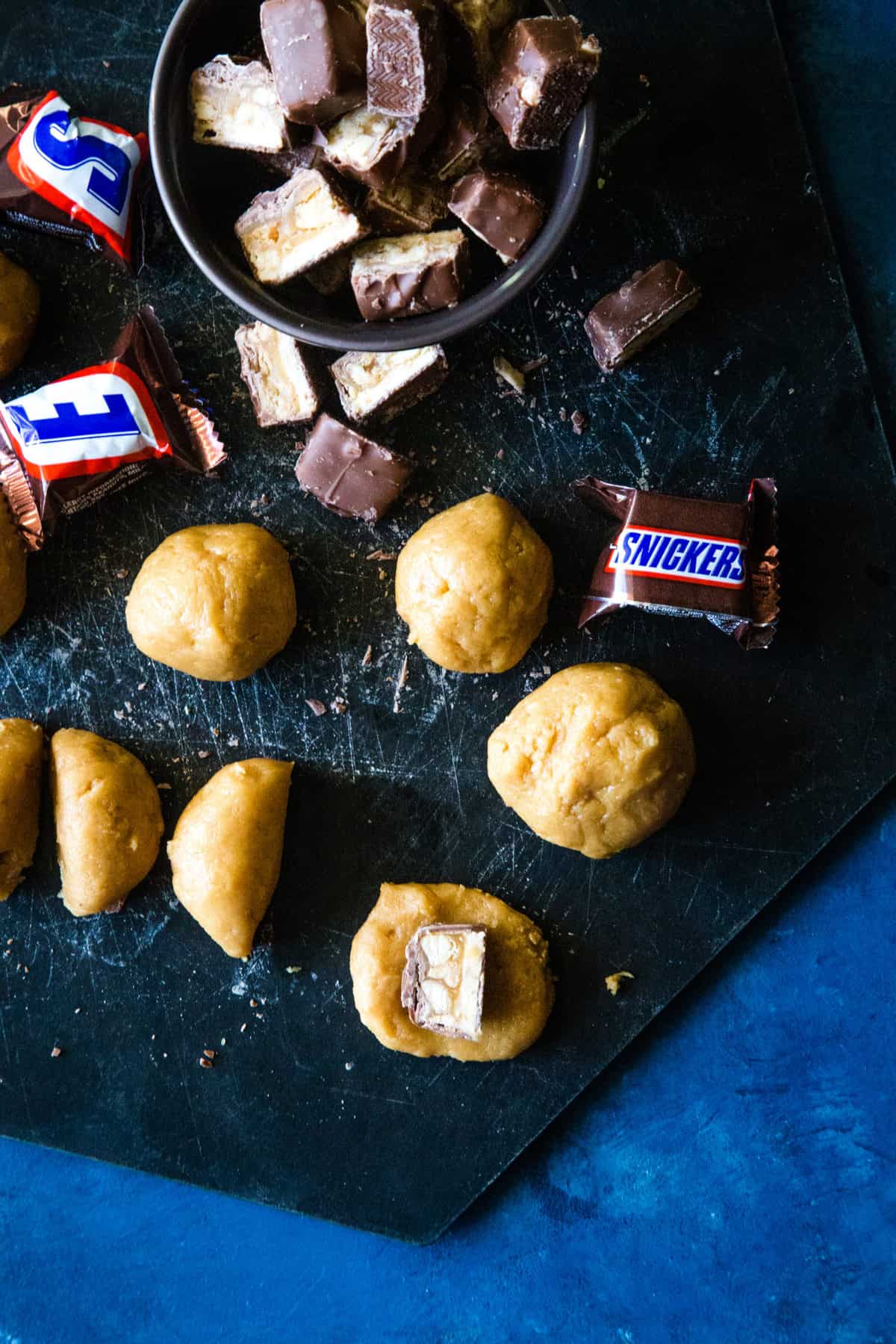 Placing half a snickers in the center of a slightly flatted cookie dough ball. 