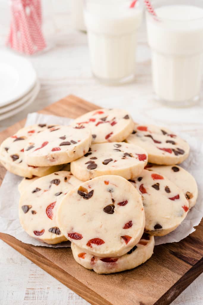 A pile of dark chocolate cherry cookies on wood cutting board with parchment paper. 