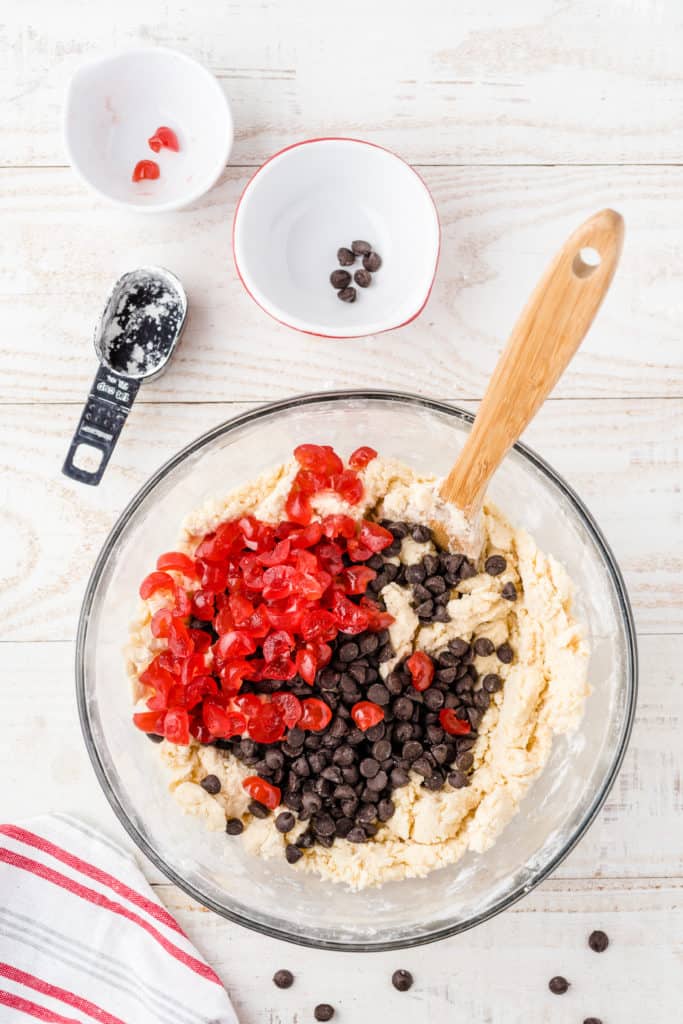 Glass bowl of shortbread dough with dark chocolate and chopped cherries. 