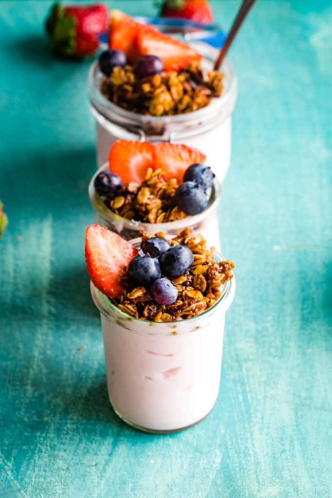 jars of yogurt parfaits with granola and fresh berries on teal background
