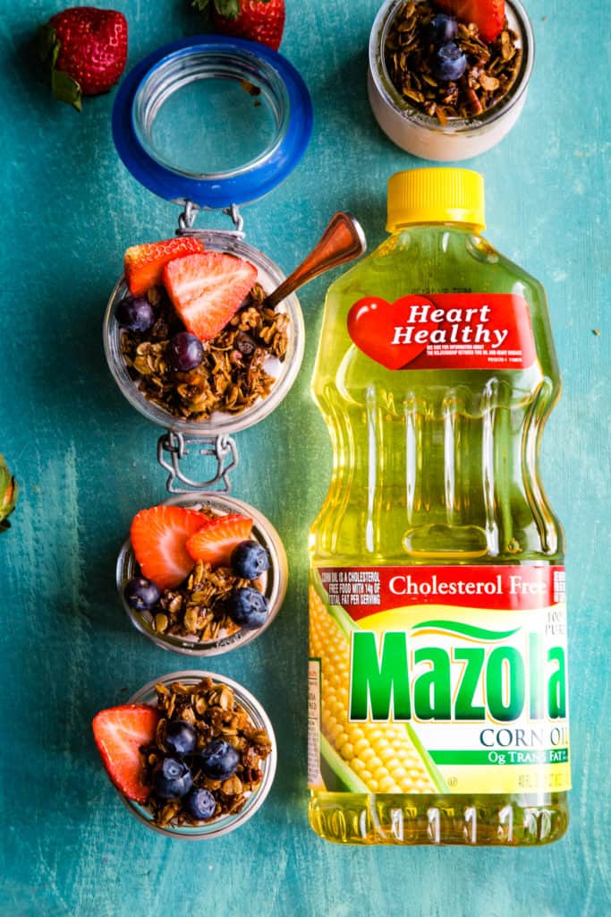 four jars of yogurt parfaits with bottle of mazola oil next to them on blue background. 