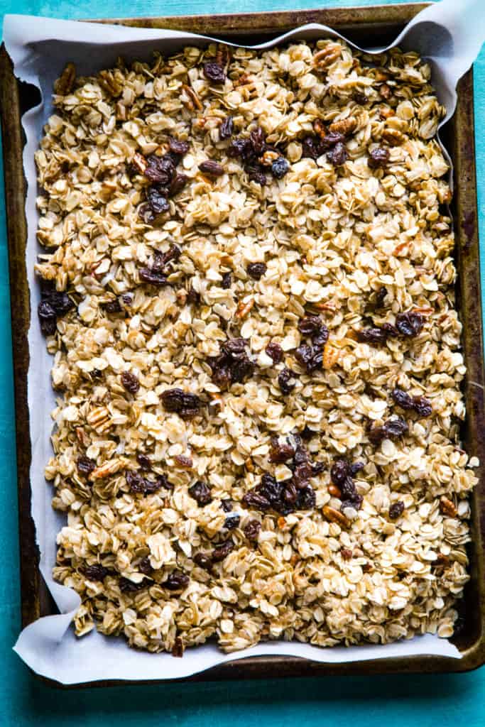 overhead shot of parchment paper lined pan full of raw granola with raisins. 