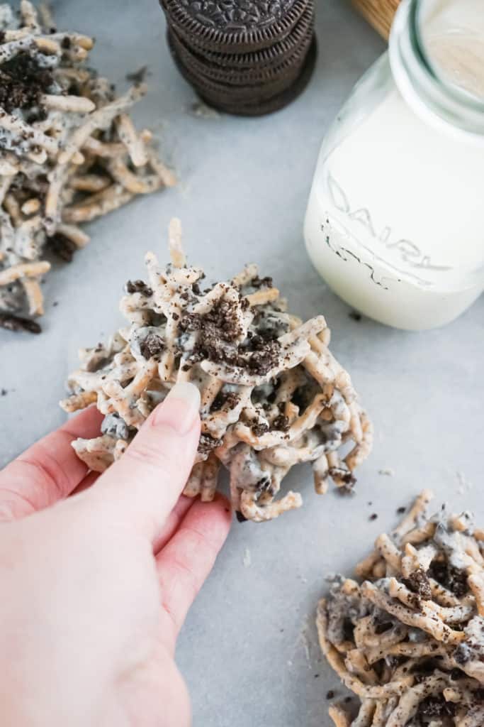 hand holding cookies and cream haystack cookie next to a jar of milk. 