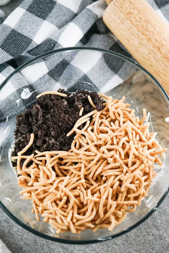 combining ingredients to make cookies and cream haystack cookies in large glass bowl with rolling pin next to it. 