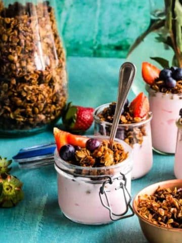 Yogurt parfaits with homemade granola in jars with strawberry yogurt on blue background.