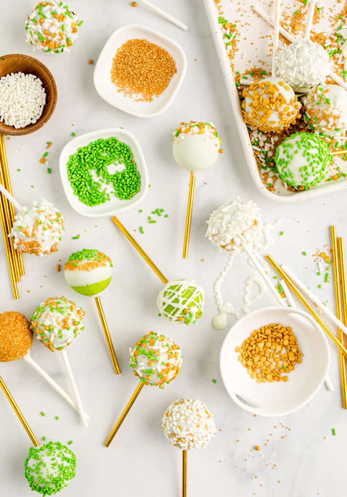 green cake pops and little bowls of sprinkles on white background