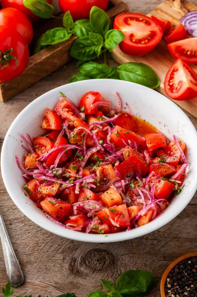 white bowl of tomato onion salad with fresh ingredients in background