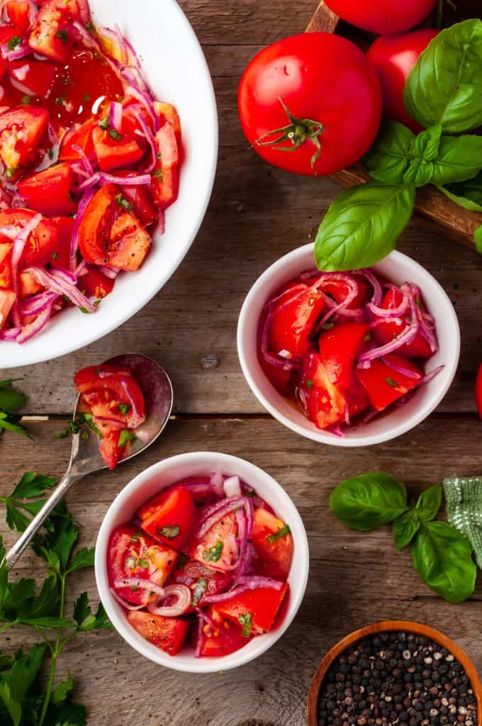 three white bowls of marinated tomato onion salad on wood background