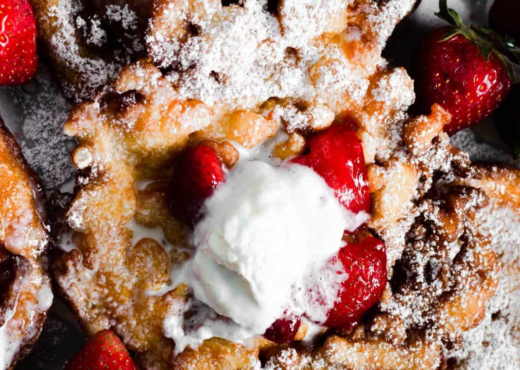 up close shot of funnel cake with strawberries and whipped cream