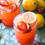 two glasses of strawberry lemonade with ice on blue background