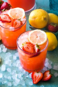 two glasses of strawberry lemonade with ice on blue background