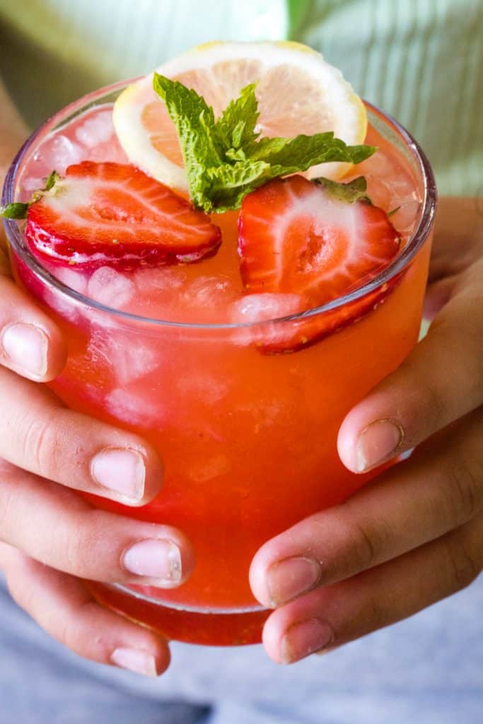 hands holding a glass of strawberry lemonade