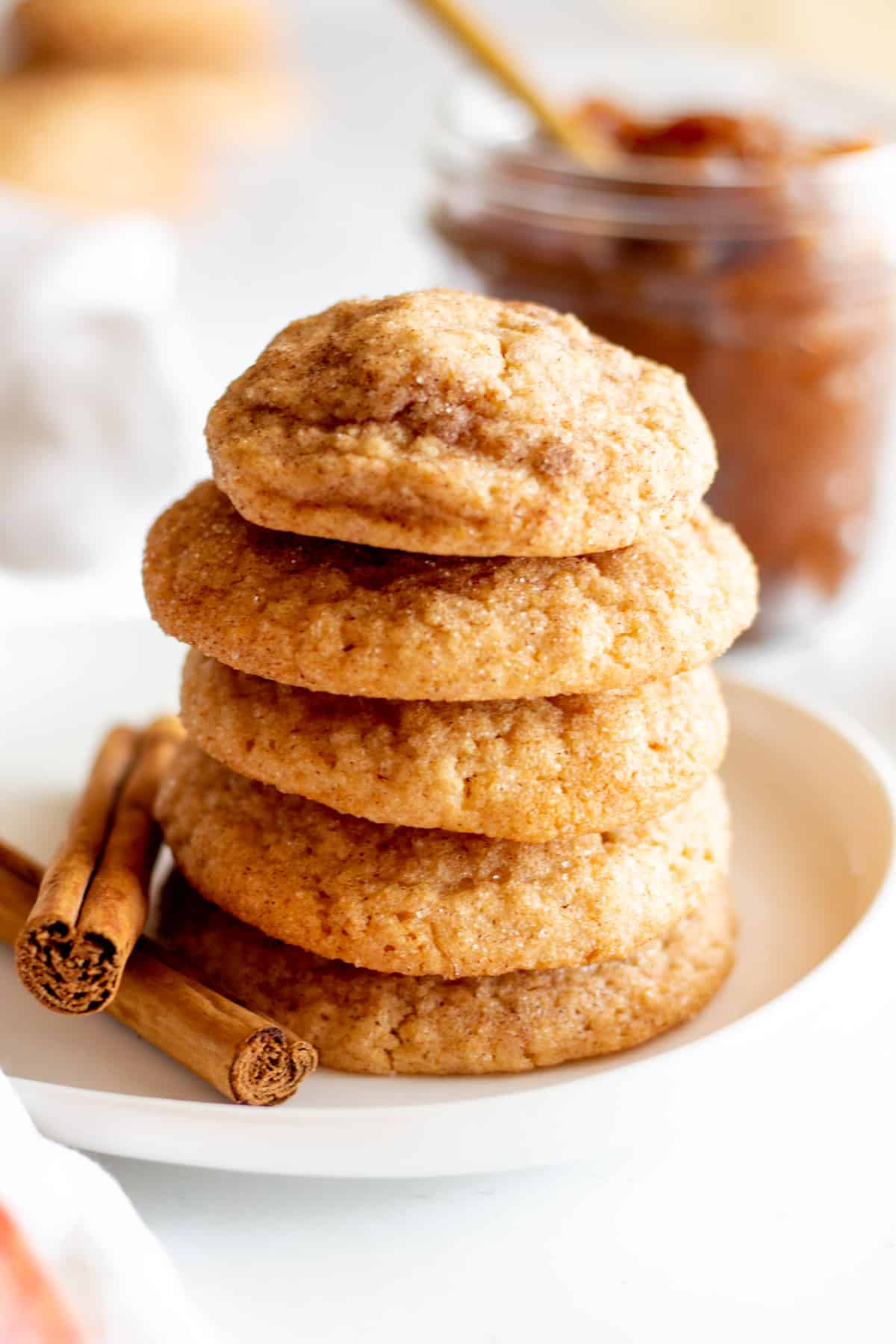 Apple butter cookies stacked on a small white plate with jar of apple butter.