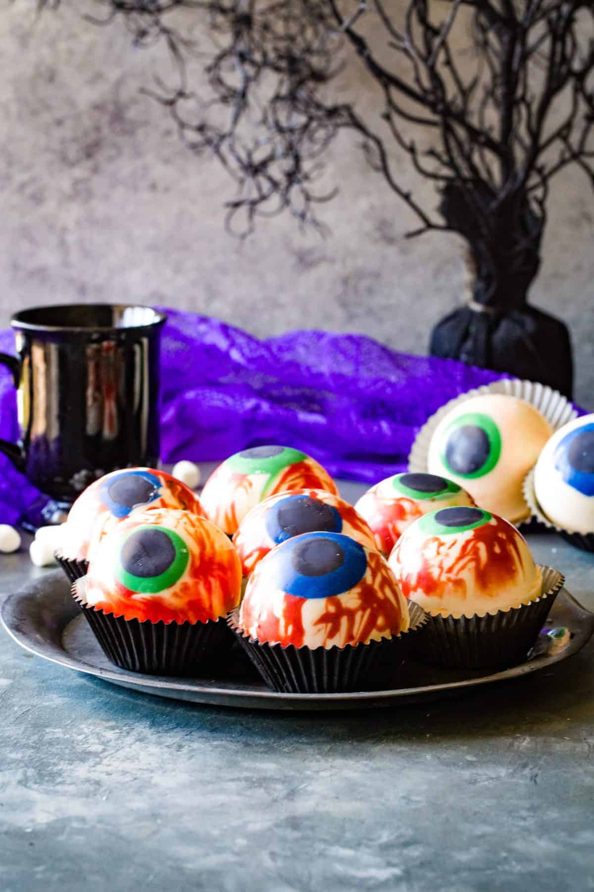 Silver plate with multiple eyeball hot cocoa bombs with purple fabric in background. 