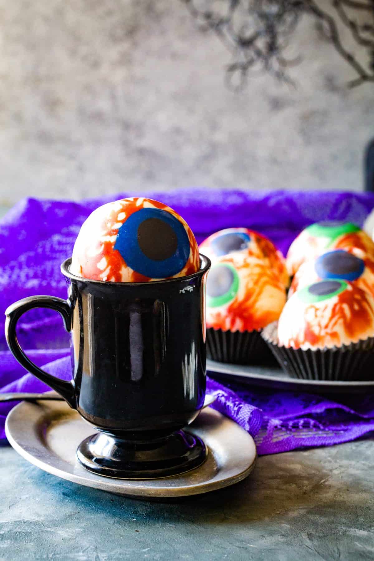 black mug with eye ball cocoa bomb over the top and plate of extras in background. 