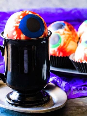 eyeball white cocoa hot chocolate bomb sitting on a black mug.