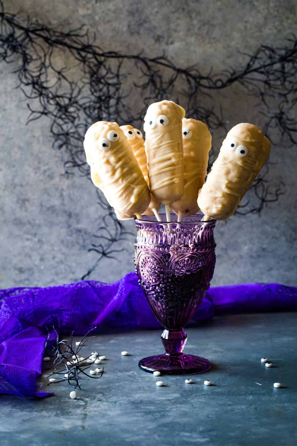 Twinkie dipped mummies on sticks in a purple glass on silver background. 