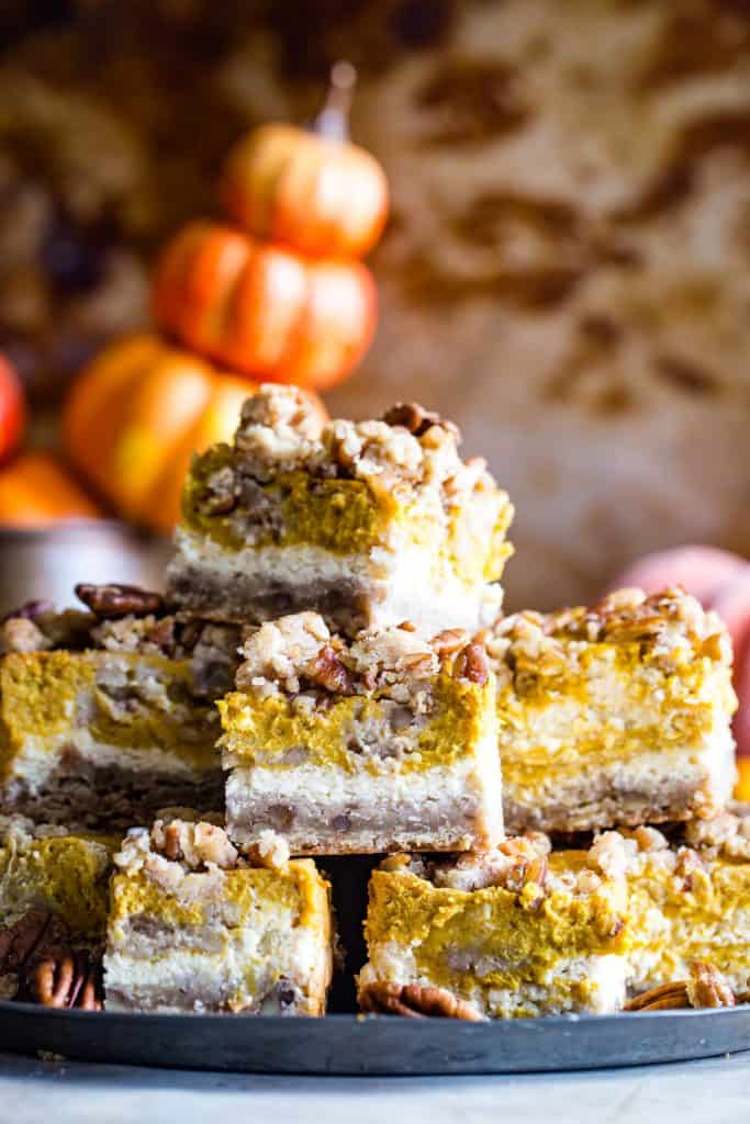 stack of pumpkin cream cheese bars with pumpkins in background