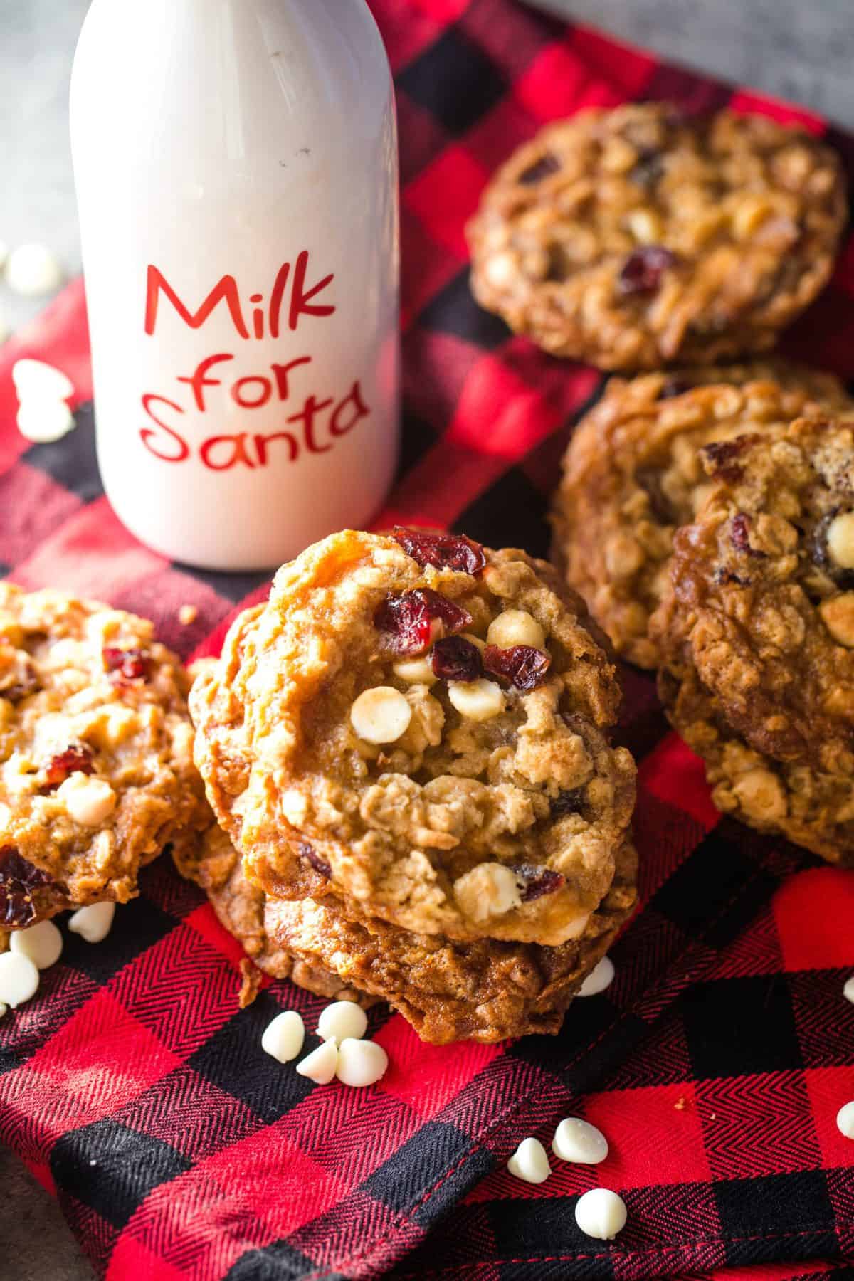 stacked white chocolate cranberry cookies on red and black flannel dishtowel with cookies for Santa jug in background