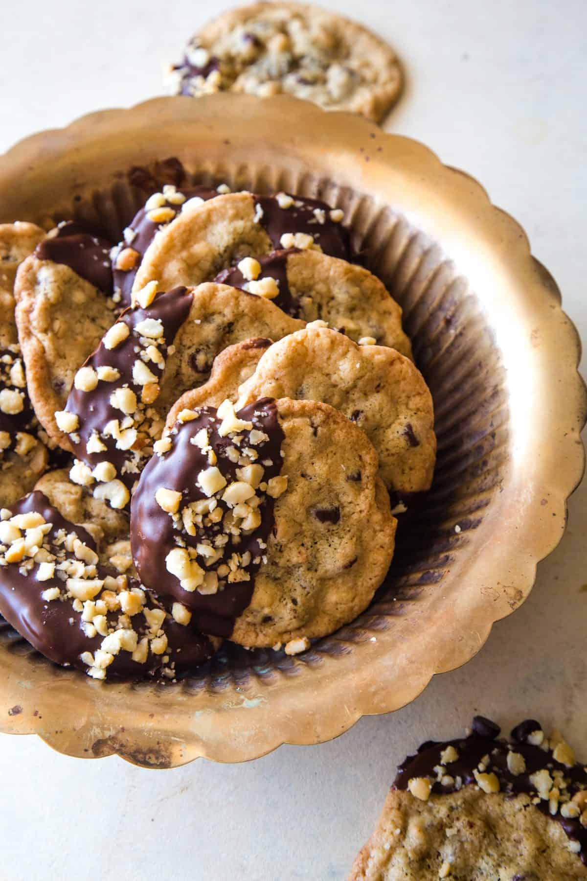 gold bowl full of chocolate dipped cookies with macadamia nuts
