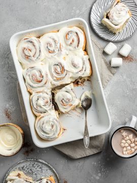 white tray of hot cocoa cinnamon rolls with icing