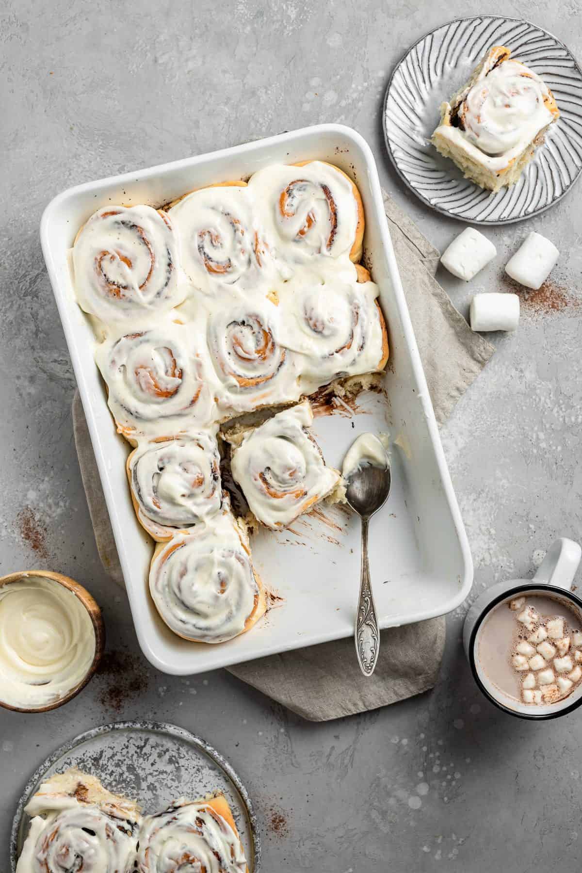 white tray of hot cocoa cinnamon rolls with icing 