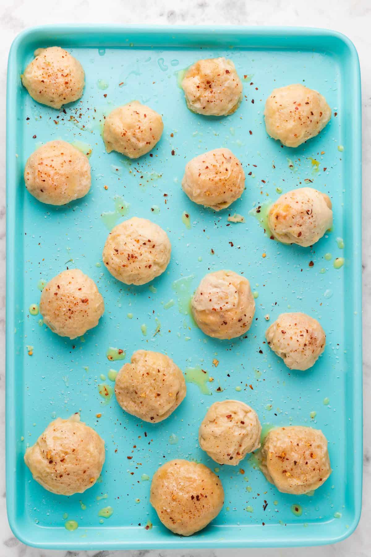 placing the boiled pretzel balls on a teal baking sheet and brushing with the melted butter mixture
