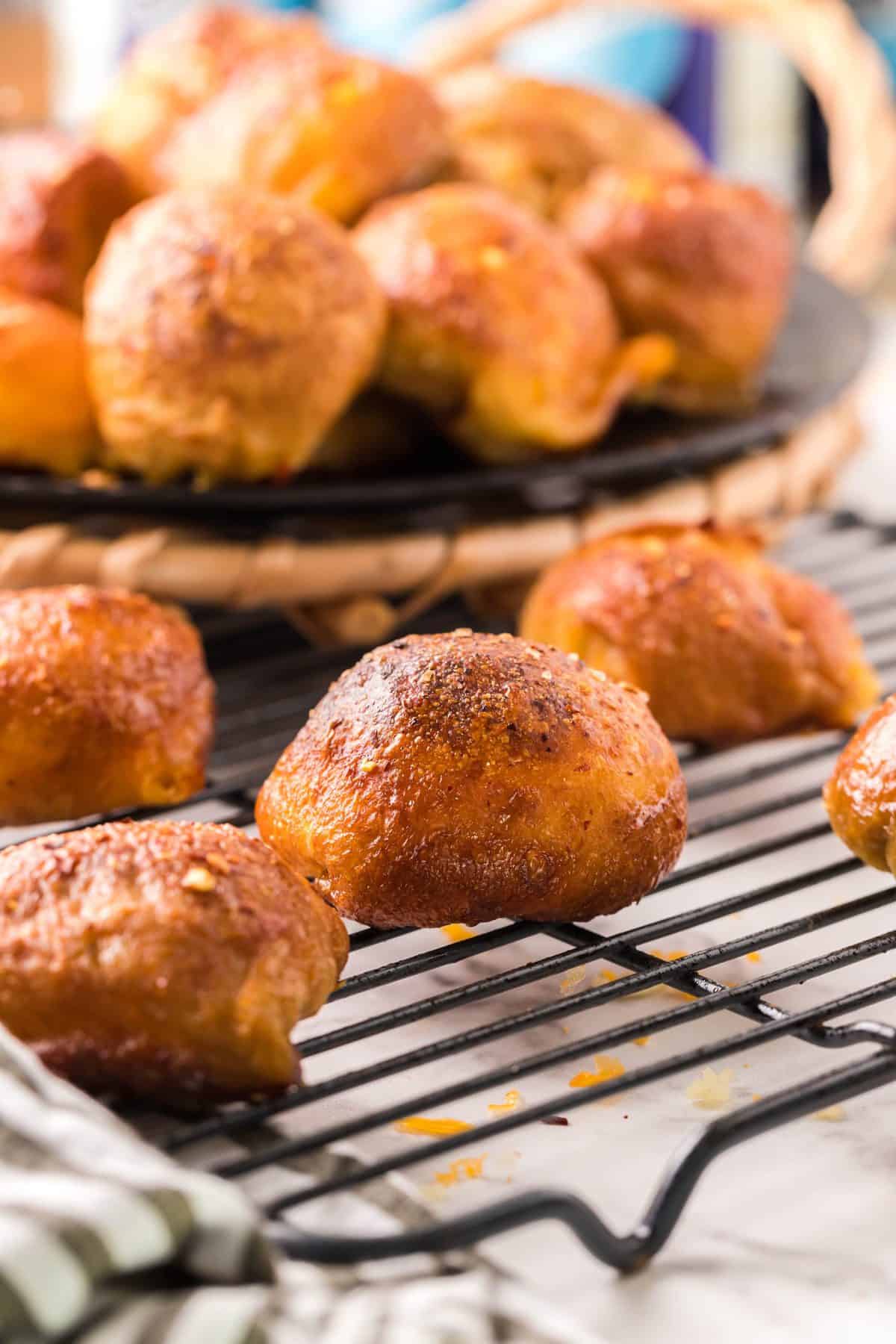 styled photo of the beer cheese pretzel balls on wire rack with plate full of rolls in the background