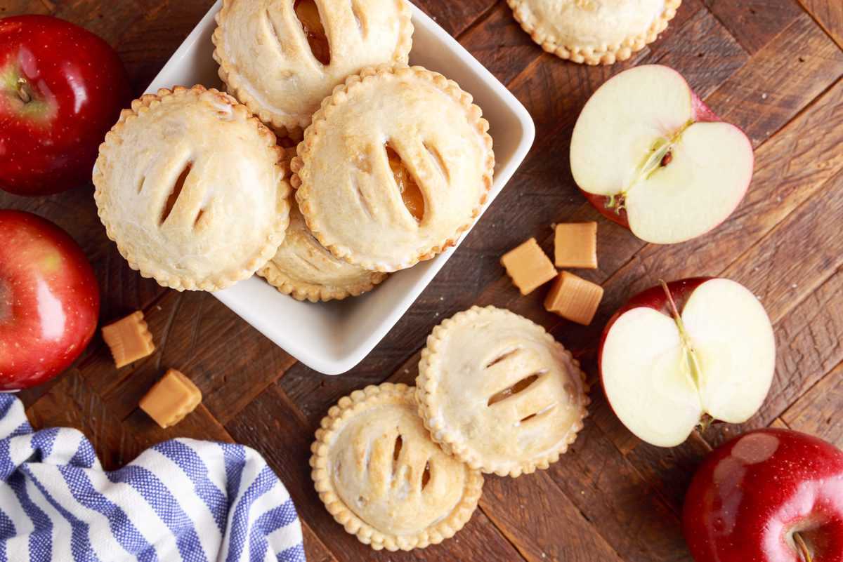 caramel apple hand pies laid out on a wood background with apples scattered around them