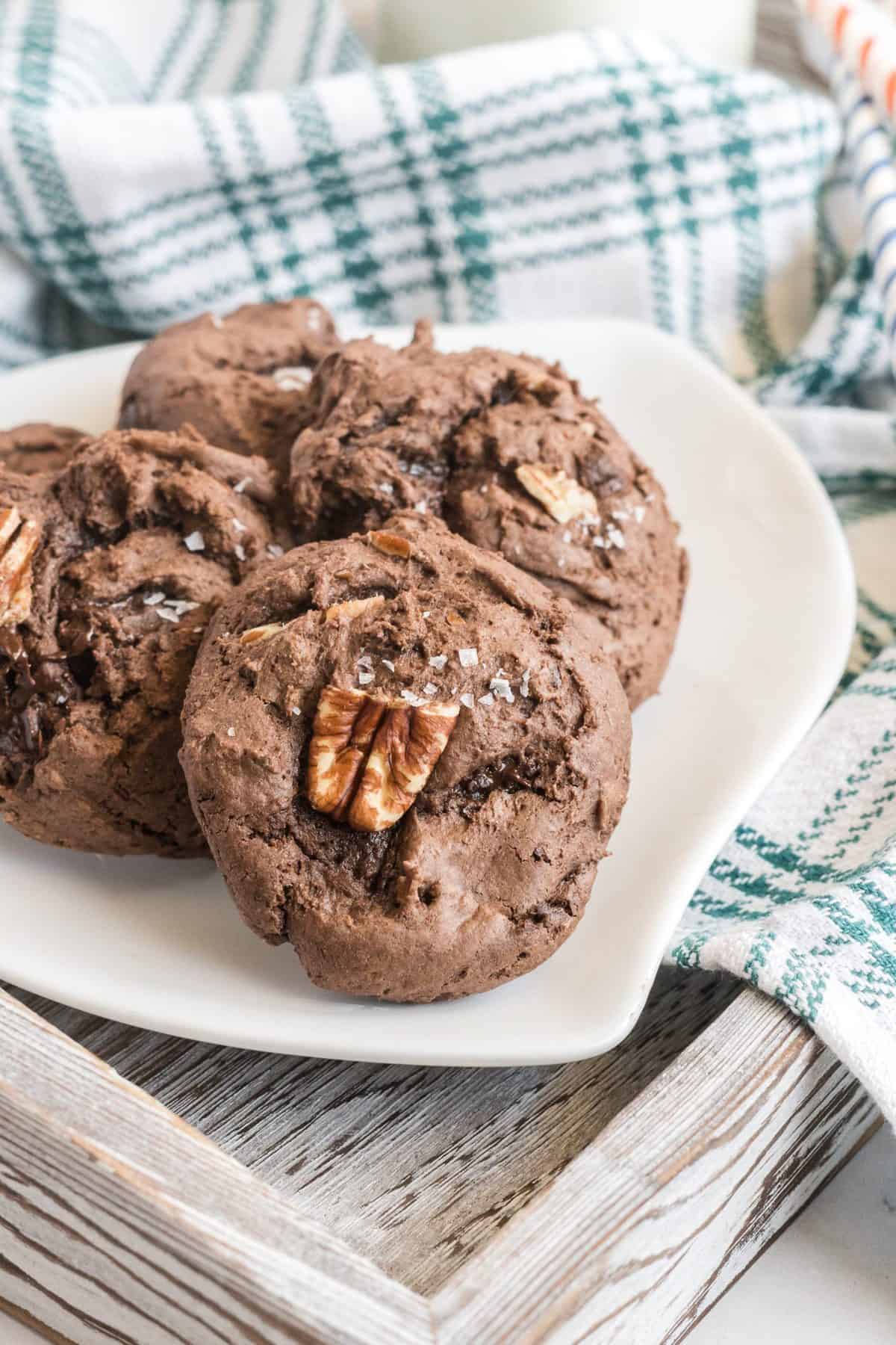 chocolate pecan cake mix cookies on a white plate with green plaid dishtowel in background. 